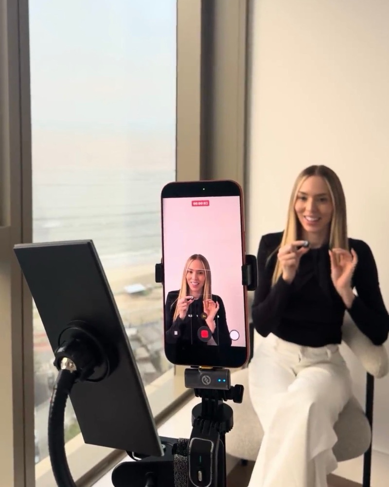 Mariana Lino gravando um vídeo de maquiagem, passando gloss com o celular no tripé